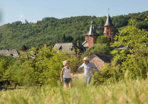 Un couple court dans un pré avec Collonges-la-Rouge à l'arrière-plan