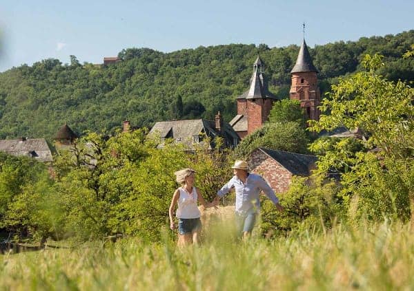 A couple running in a meadow with Collonges-la-Rouge in the background