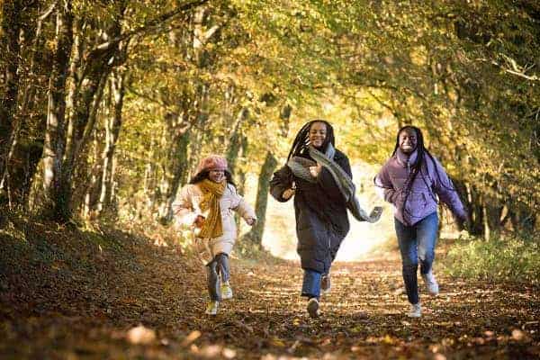 Three young girls run along a path in the woods
