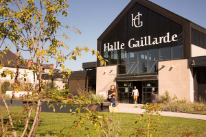Vue sur l'extérieur de la Halle gaillarde. Un couple est assis sur un banc devant l'entrée