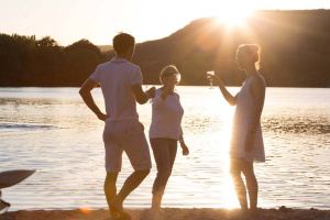 Deux femmes et un homme trinquent sur la plage du lac du Causse au soleil couchant