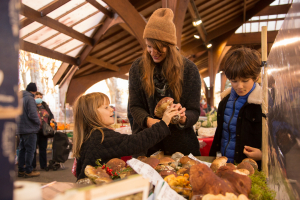 Mère qui achète des champignons avec ses enfants et qui montre à quoi ce gros champignon ressemble à sa fille