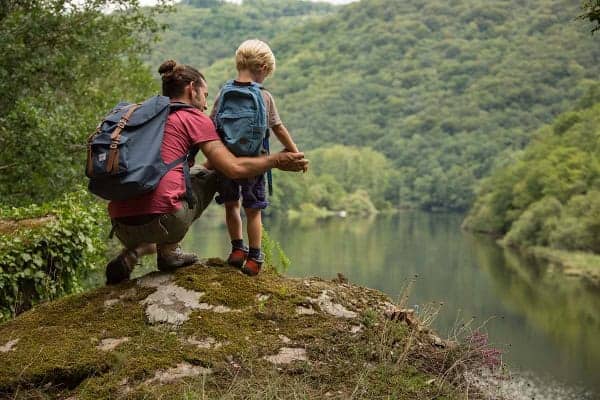 Un père et son petit garçon sont debouts sur un rocher face à un paysage vallonné, typique de la Xaintrie