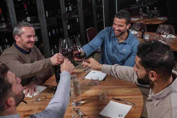 Vier jongens zitten aan tafel en drinken een toast