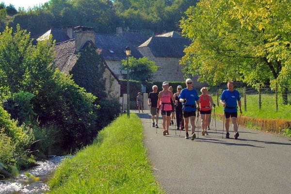 Un groupe de randonneur équipés de bâtons marchent sur une route de campagne