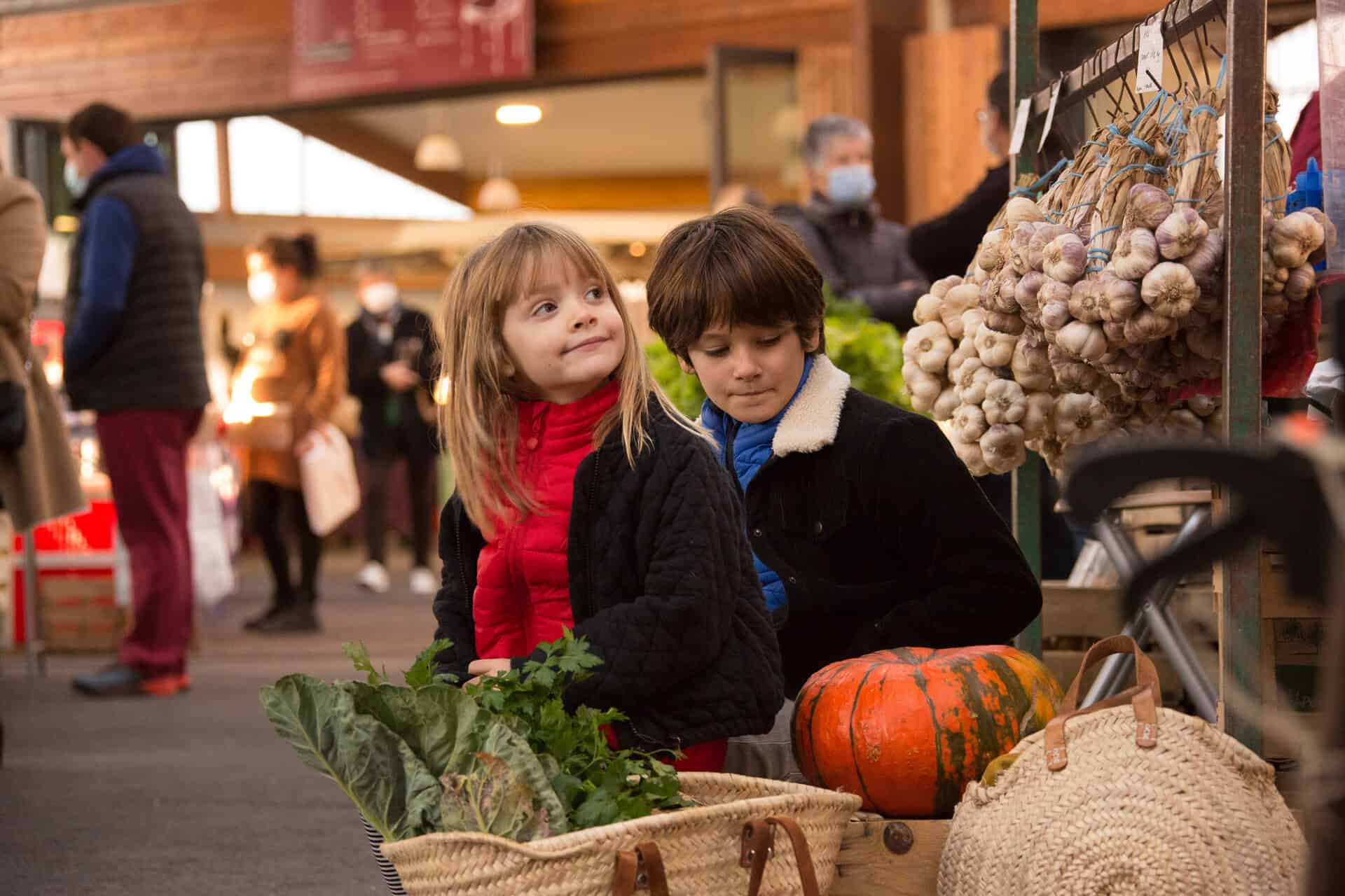 Twee kinderen op de markt van Brive-La-Gaillarde op een herfstzaterdag, voor een rij pompoenen.